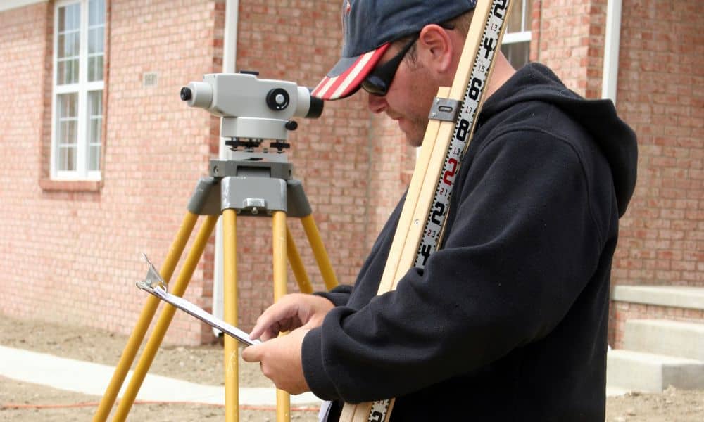 Surveyor measuring home elevation with tripod equipment for a FEMA elevation certificate