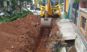 Excavator digging a trench near a residential property line, highlighting the importance of a boundary survey before starting construction.