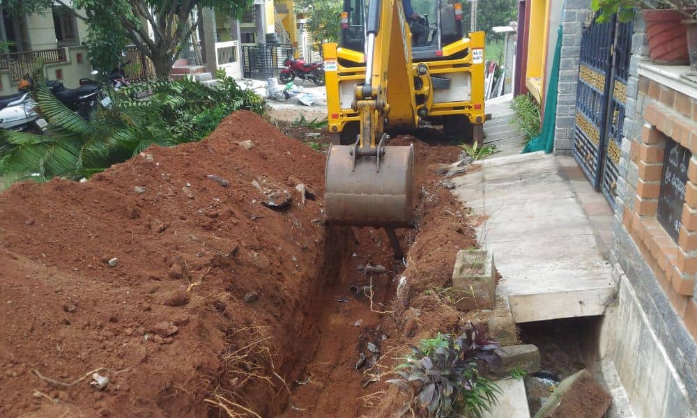 Excavator digging a trench near a residential property line, highlighting the importance of a boundary survey before starting construction.