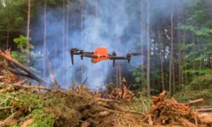 Drone surveying over a forest with smoke rising from wildfire debris