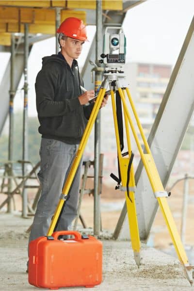 Licensed land surveyor using surveying equipment at a construction site to monitor land elevation and detect ground sinking.
