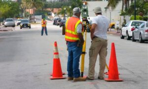 Surveyors using total station equipment beside traffic cones on a closed roadway for an alta land title survey