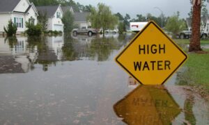 Flooded suburban neighborhood with a high water warning sign illustrating why accurate data from a loan closing survey is vital during the NFIP freeze
