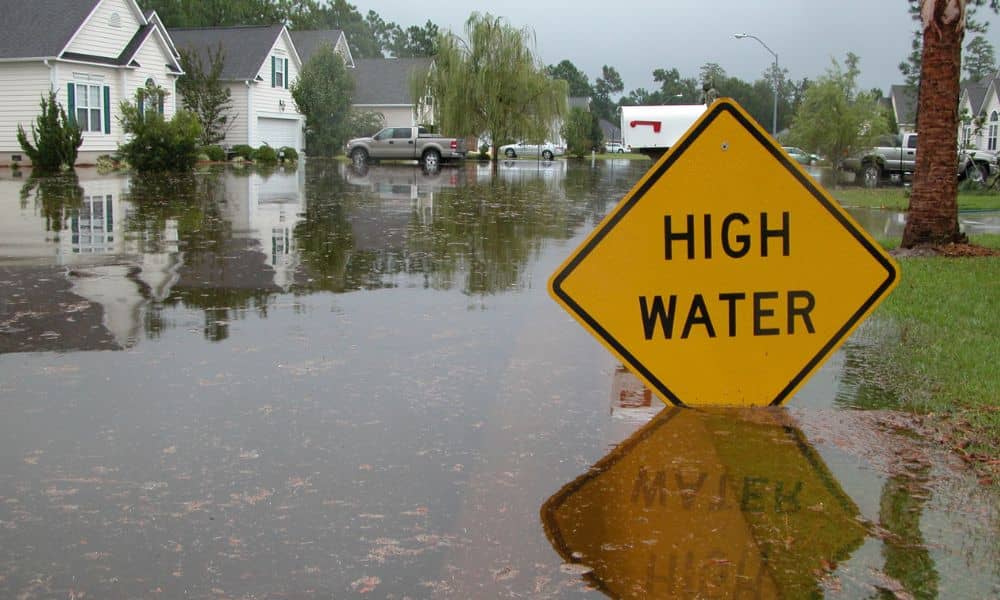 Flooded suburban neighborhood with a high water warning sign illustrating why accurate data from a loan closing survey is vital during the NFIP freeze

