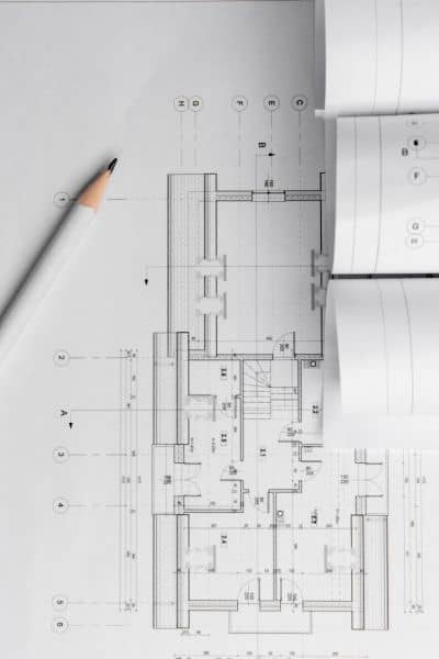 A detailed architectural blueprint with a pencil and rolled plans, showing the technical documents surveyors reference during a property survey