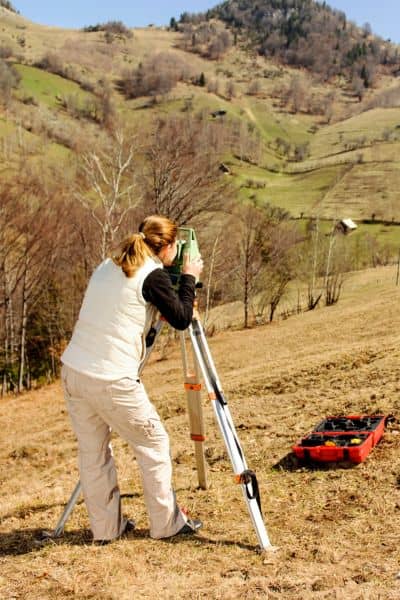 Surveyor using equipment on a hillside to capture elevation data for a topographic survey