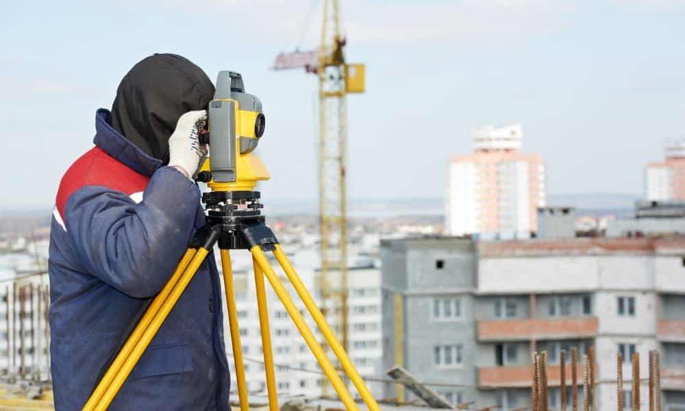 A land surveyor using a total station on a city construction site while preparing measurements for a property survey