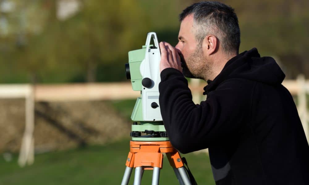 Licensed land surveyor conducting a boundary survey near a fence to verify legal property lines during a land dispute